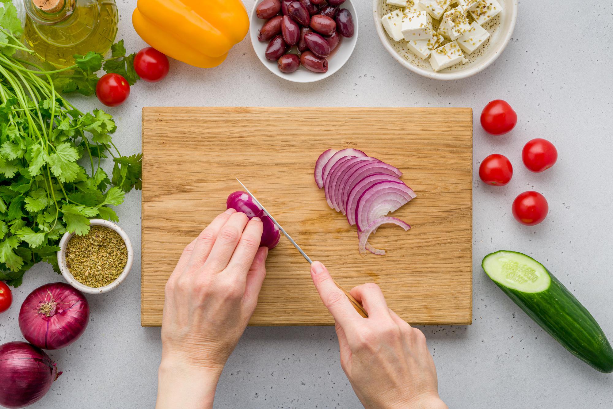 Hands slicing seasonal vegetables on marble